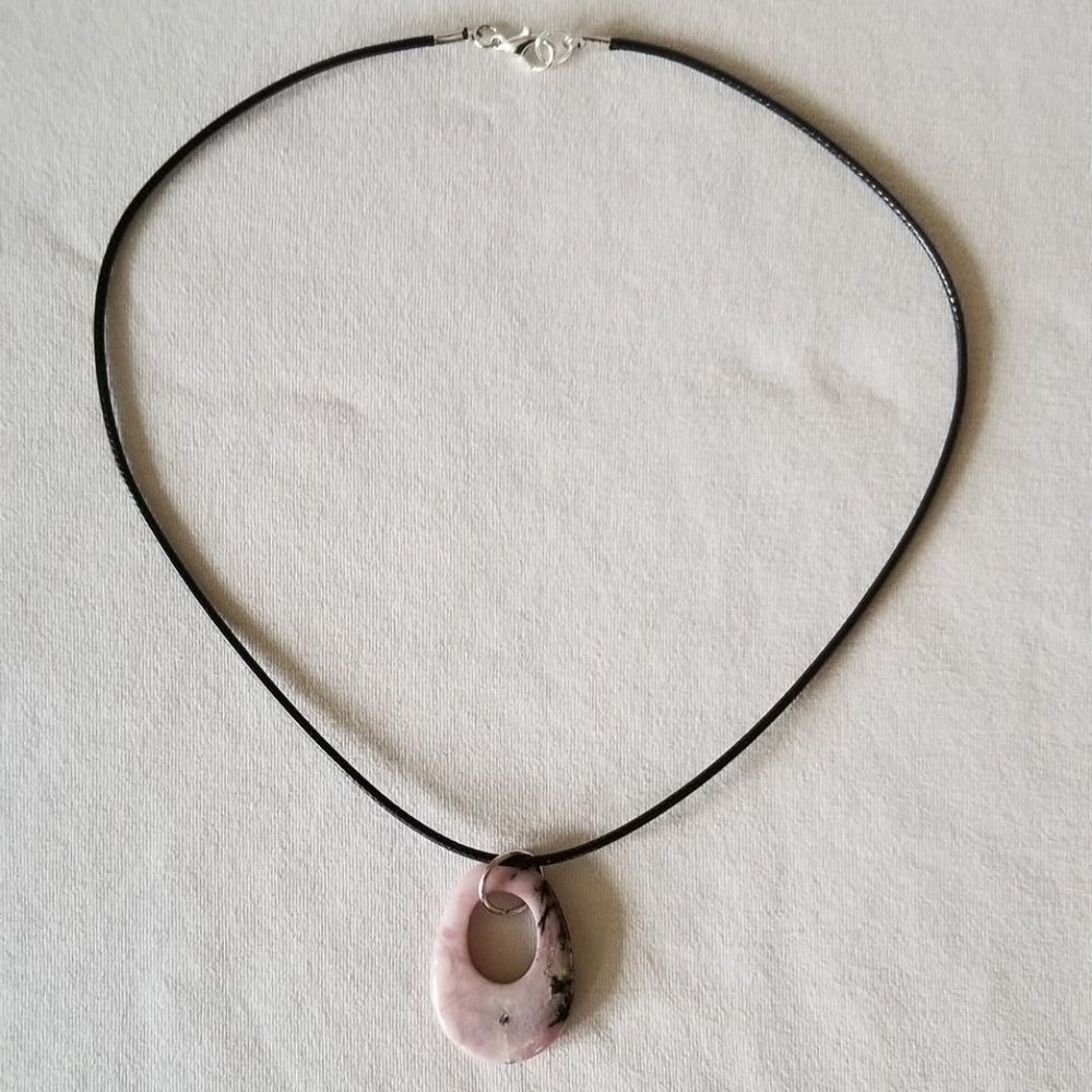 Pink rhodonite gemstone with black veining, natural pendant on a black cord.